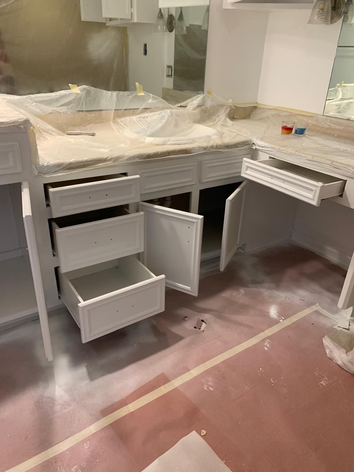White painted cabinets with open drawers and doors in a room. Red painted floor.