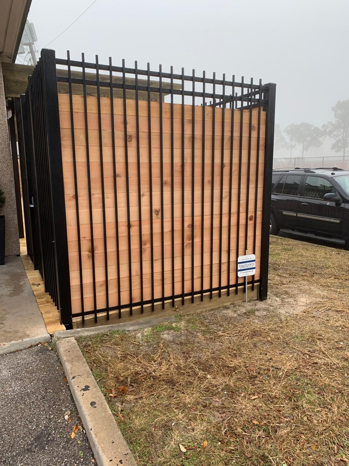 Black metal and wood panel fence in front of a building and grassy area.