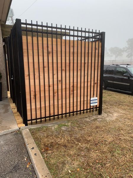 Black metal and wood panel fence in front of a building and grassy area.