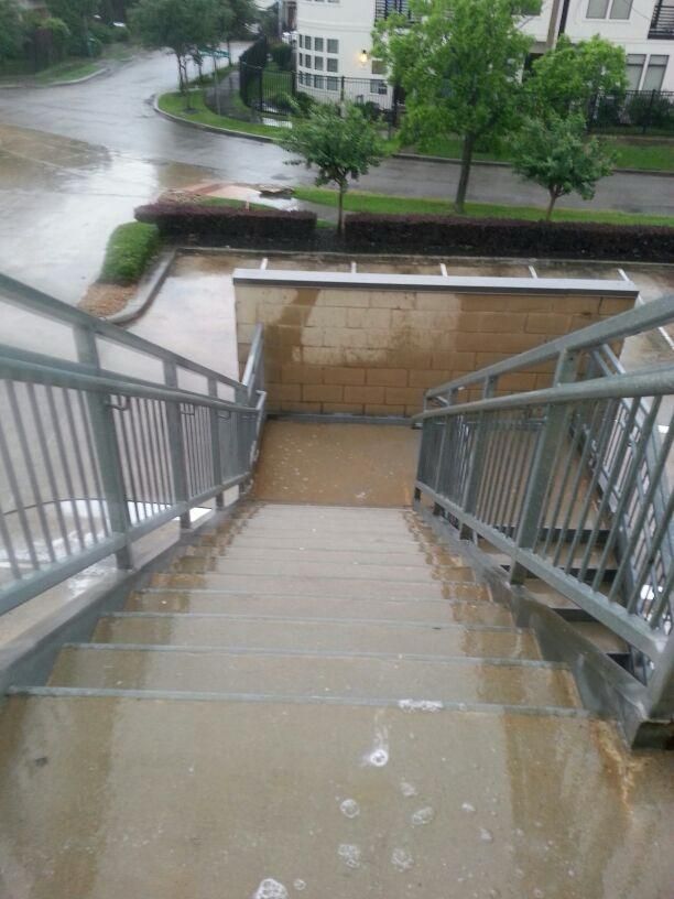 Staircase leading down, wet from rain. Grey metal handrails, beige wall at landing, street in background.