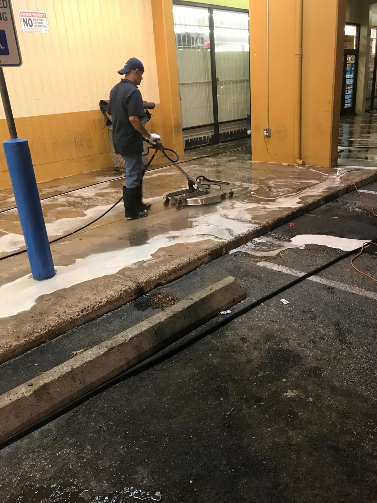 Person using a pressure washer to clean a wet concrete floor at a car wash.