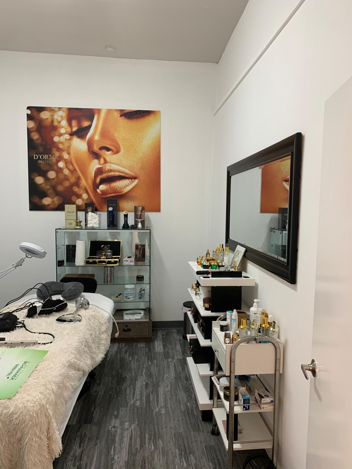 A beauty treatment room with a bed, shelves of products, a large mirror, and a woman's face poster.