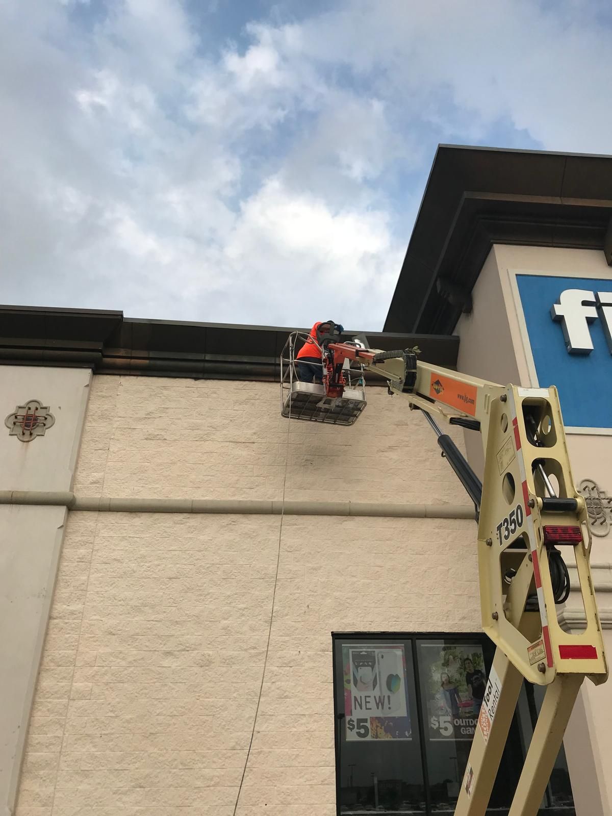 Person in a cherry picker working on the exterior of a building, under a cloudy sky.