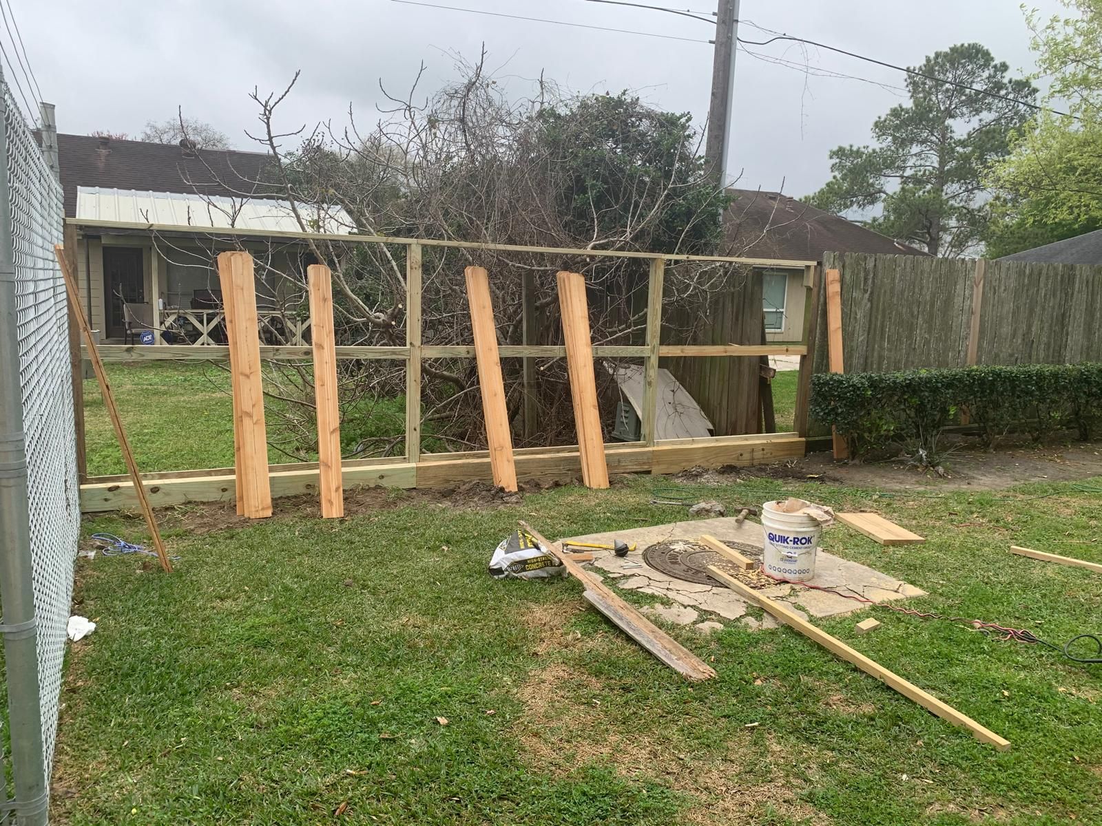 Fence under construction; wooden posts and framework set in backyard with tools on the grass.