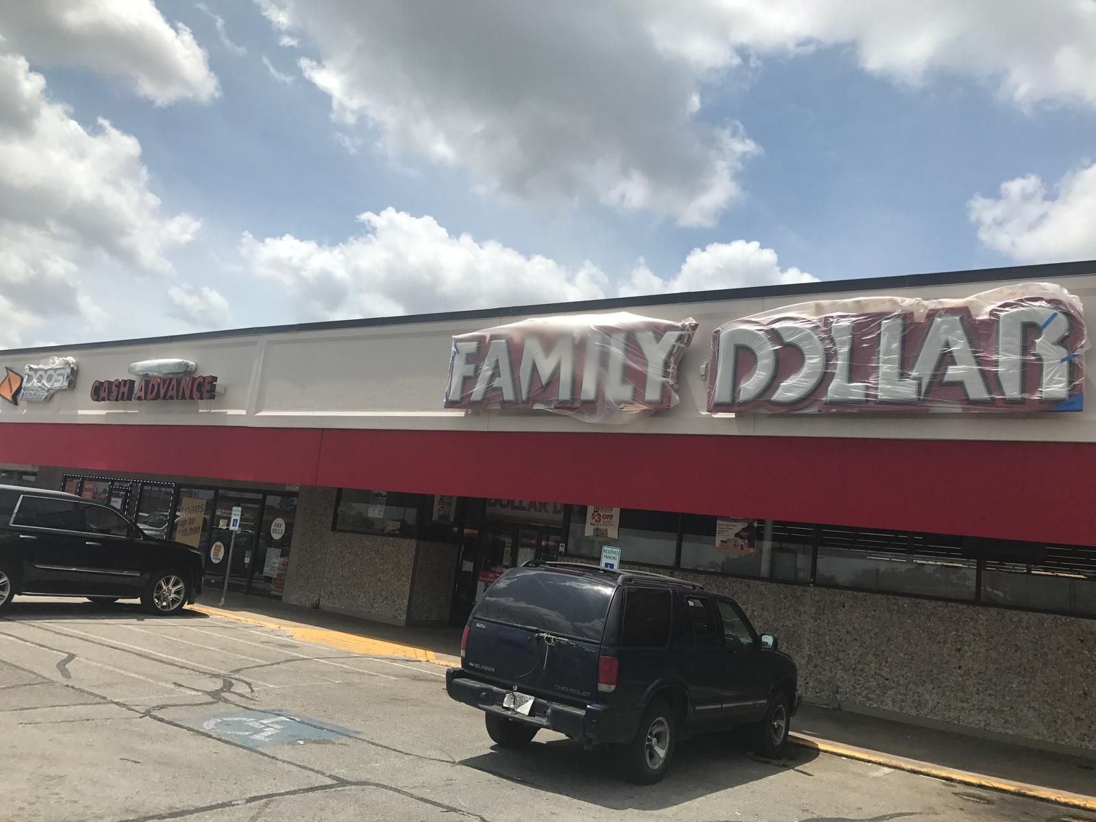Family Dollar store with red awning and a car in front. Cloudy sky.