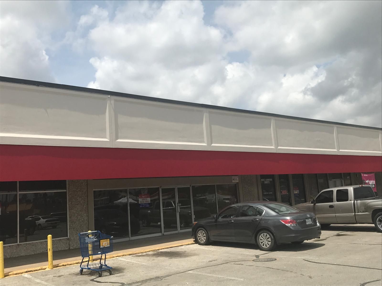 Storefront with red awning, gray car parked in front, shopping cart, cloudy sky.