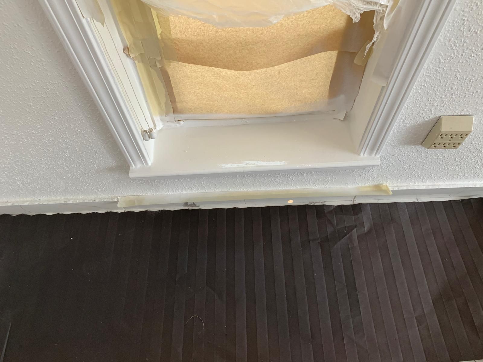 White alcove with plastic covering, brown textured floor, and white textured wall.