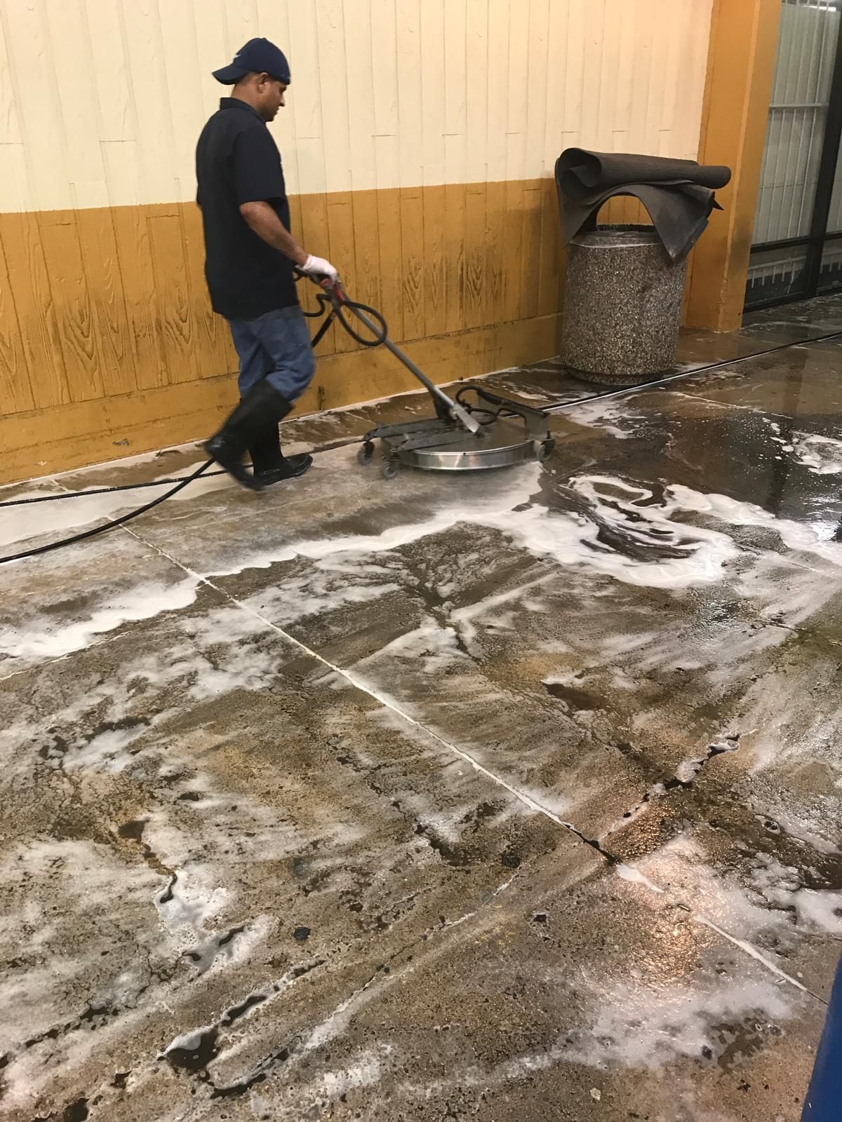 Man pressure washing a concrete floor with soapy water.