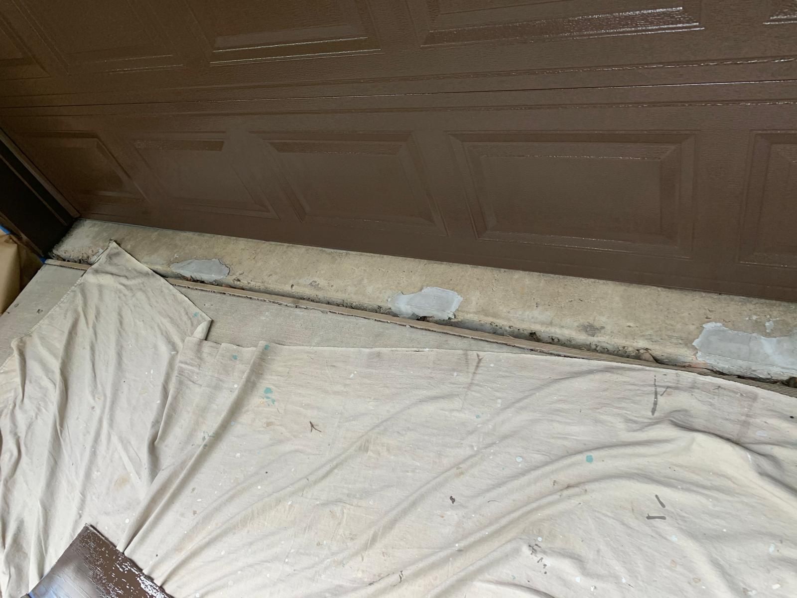A concrete floor with a crack near a brown garage door, covered by a drop cloth.