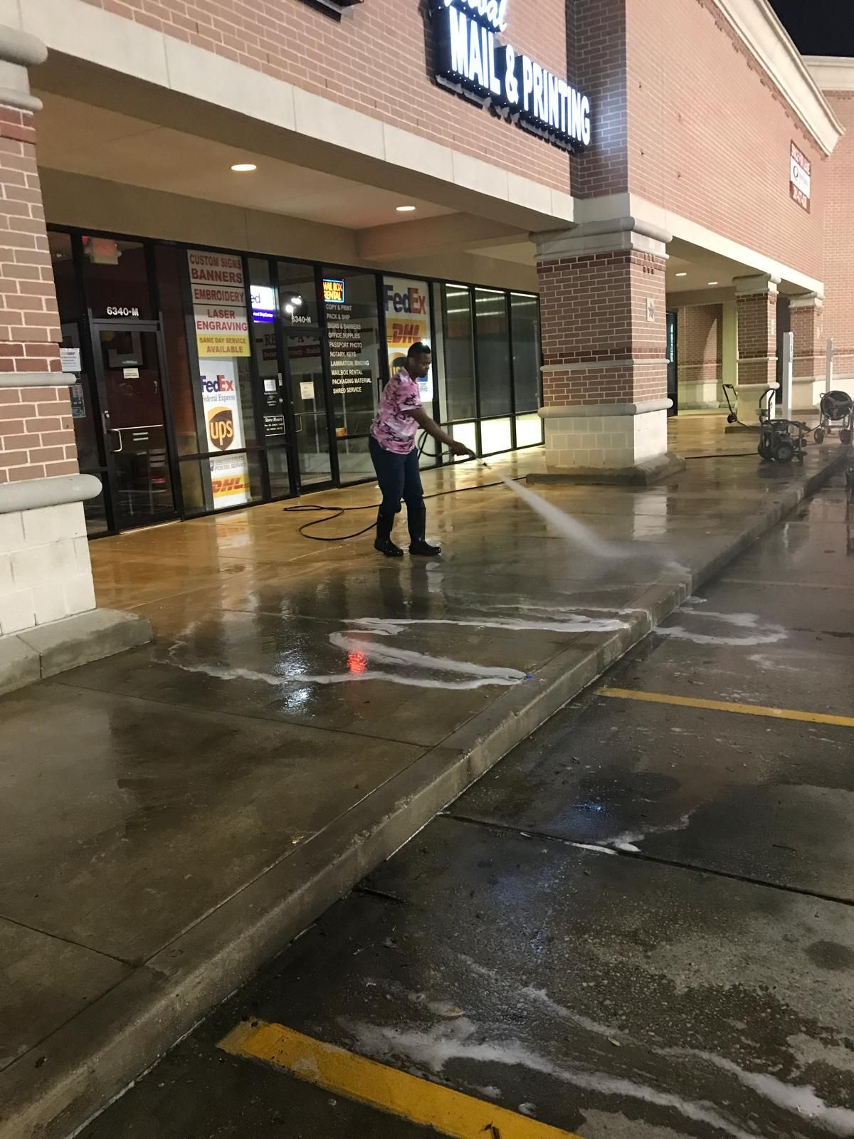Person pressure washing the sidewalk in front of a brick building at night.