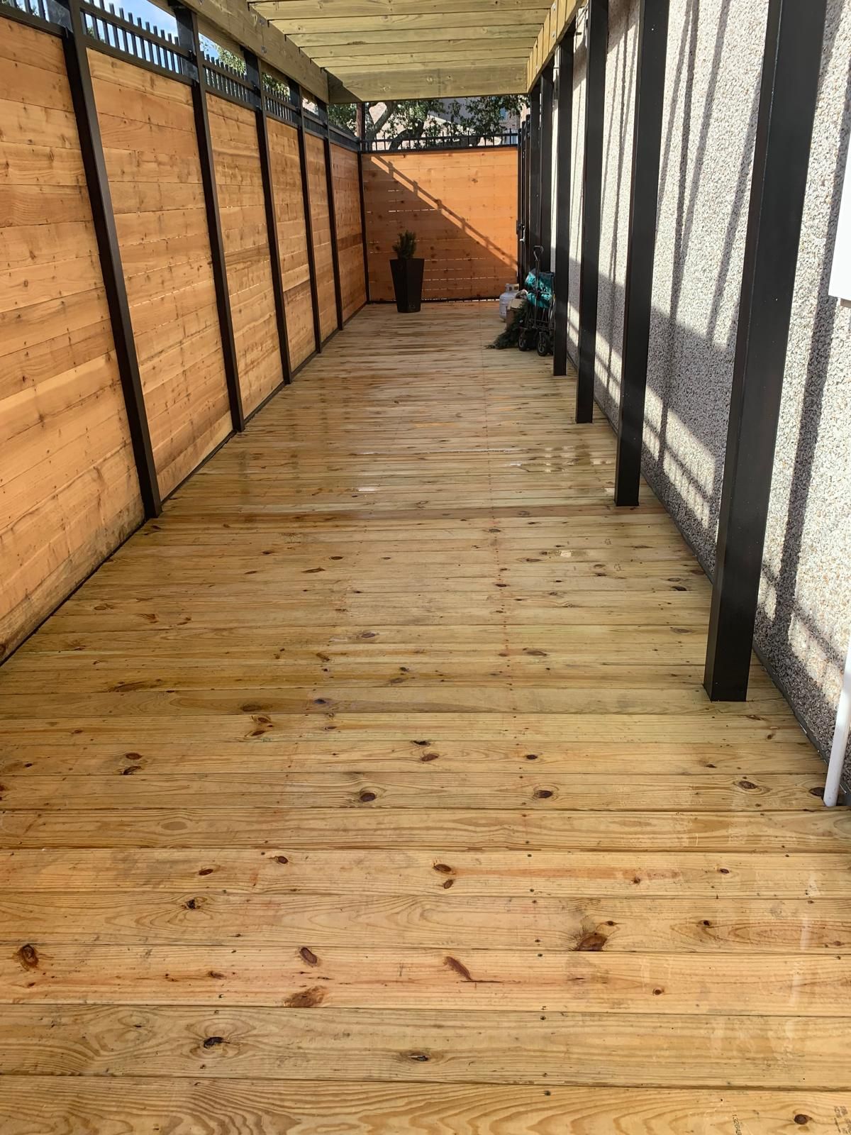 Wooden walkway with fence and shade structure. Sunlight on the wood.