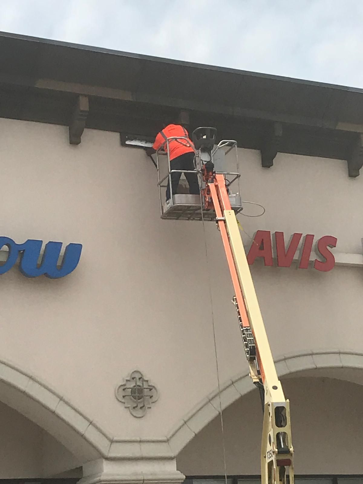 Worker in orange vest in a lift basket, working on building's awning. 