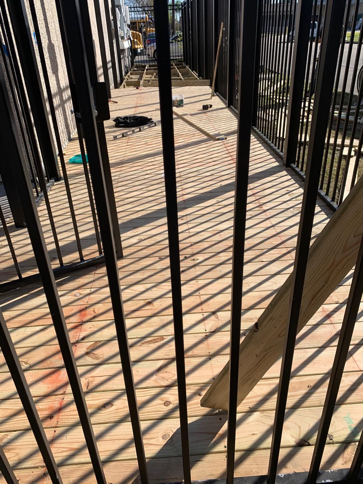 Wooden walkway with black metal railing; sunlight casts shadows on the boards.
