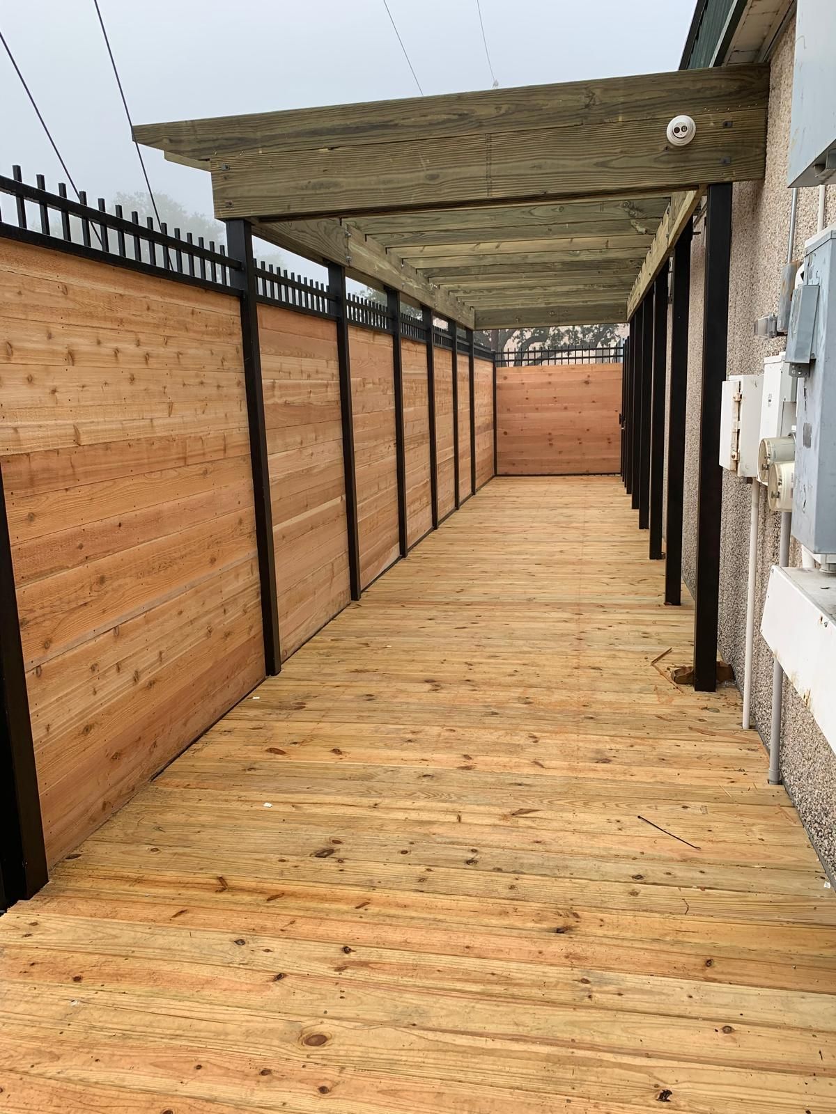 Wooden walkway with cedar fence and pergola along a building.
