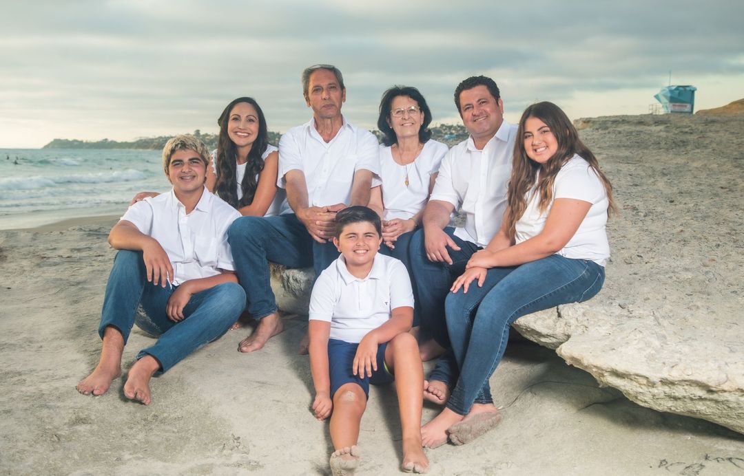 A family is sitting on a rock on the beach.