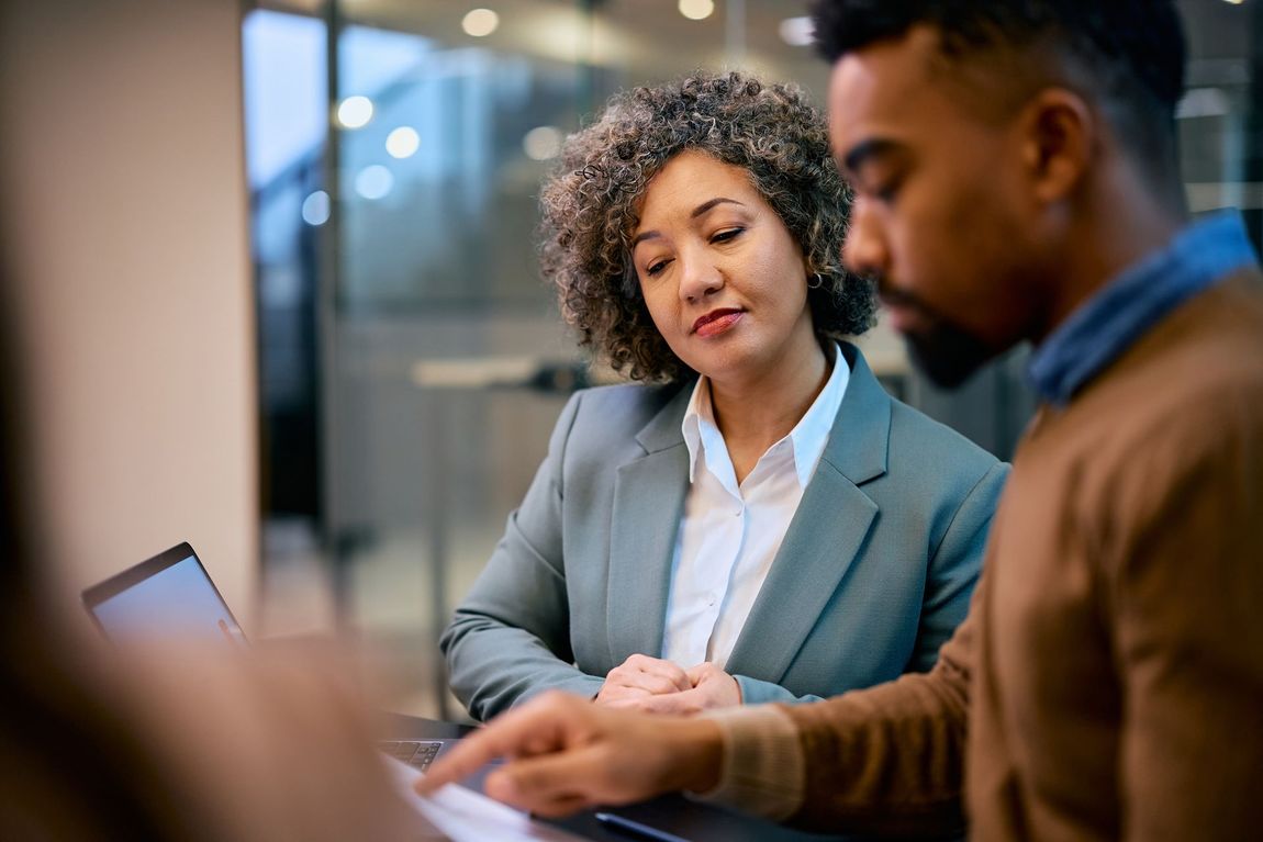 A man and a woman are sitting at a table looking at a laptop.