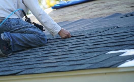 A man is kneeling on a roof while working on it.
