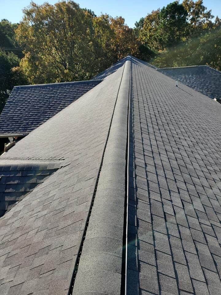 A close up of a roof with a gutter and trees in the background.