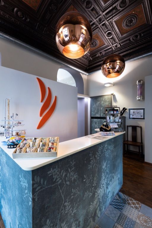 Area reception con bancone bianco, logo arancione, lampade in rame e carta da parati a motivi.