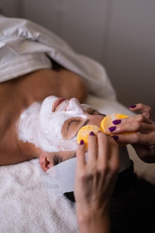 Persona che riceve un trattamento viso; viene applicata una maschera di crema bianca, le mani tengono delle spugne.