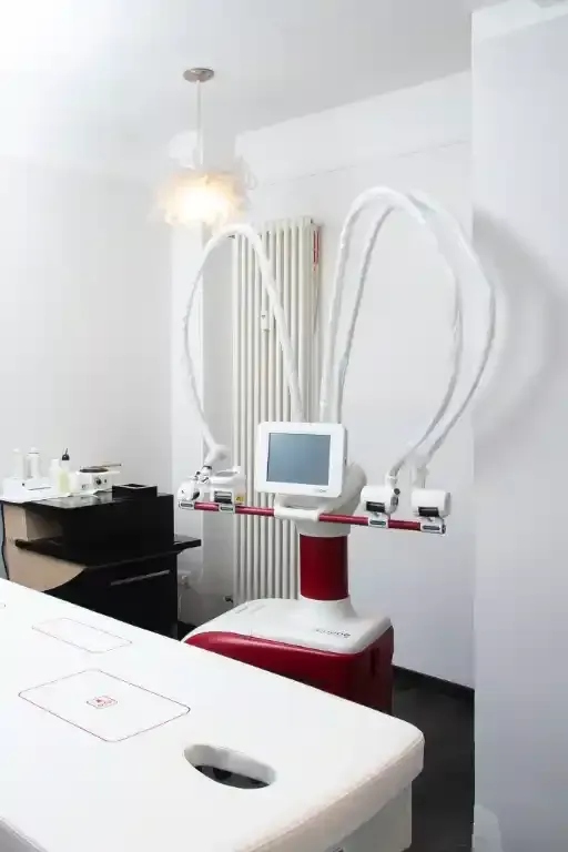 Studio medico: Apparecchio per trattamenti laser con lettino, monitor e bracci flessibili bianchi, accanto a un termosifone.