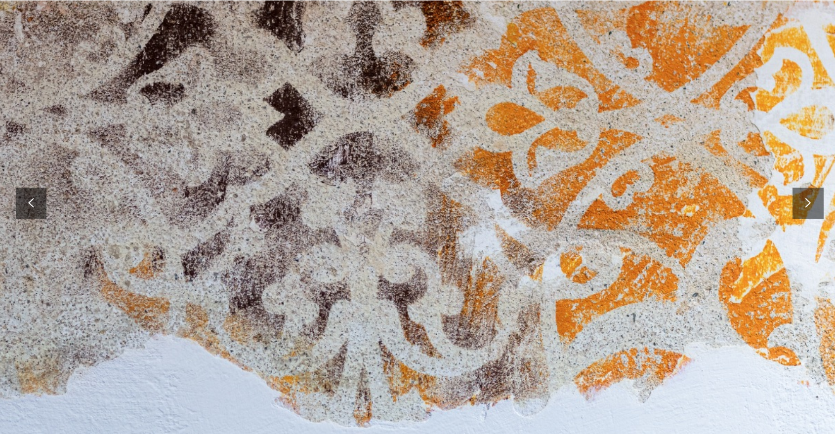 Parete rovinata che presenta un motivo ornato e sbiadito in marrone e arancione su una base bianca.