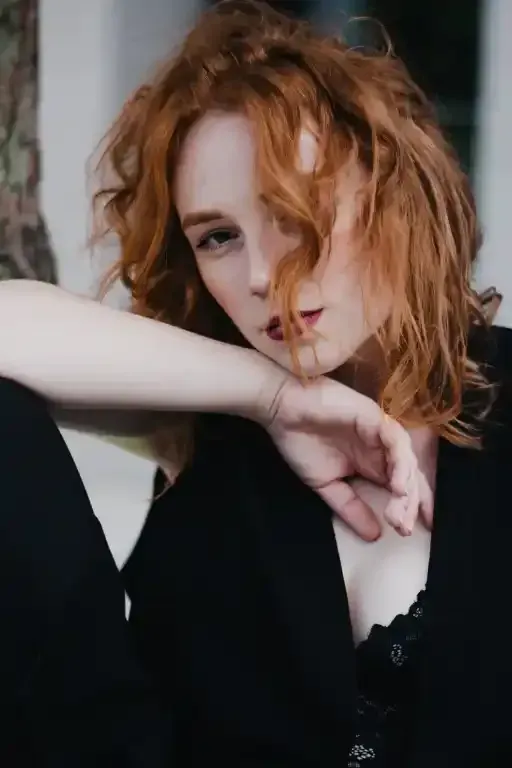 Donna con i capelli rossi, mento appoggiato sulla mano. Indossa un top nero.