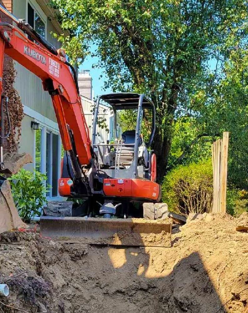 A red excavator is digging a hole in the dirt in front of a house.