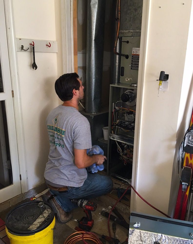A man is working on an air conditioner in a garage.