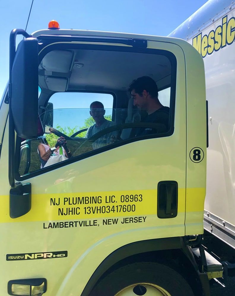 Two men are sitting in the driver 's seat of a nj plumbing truck