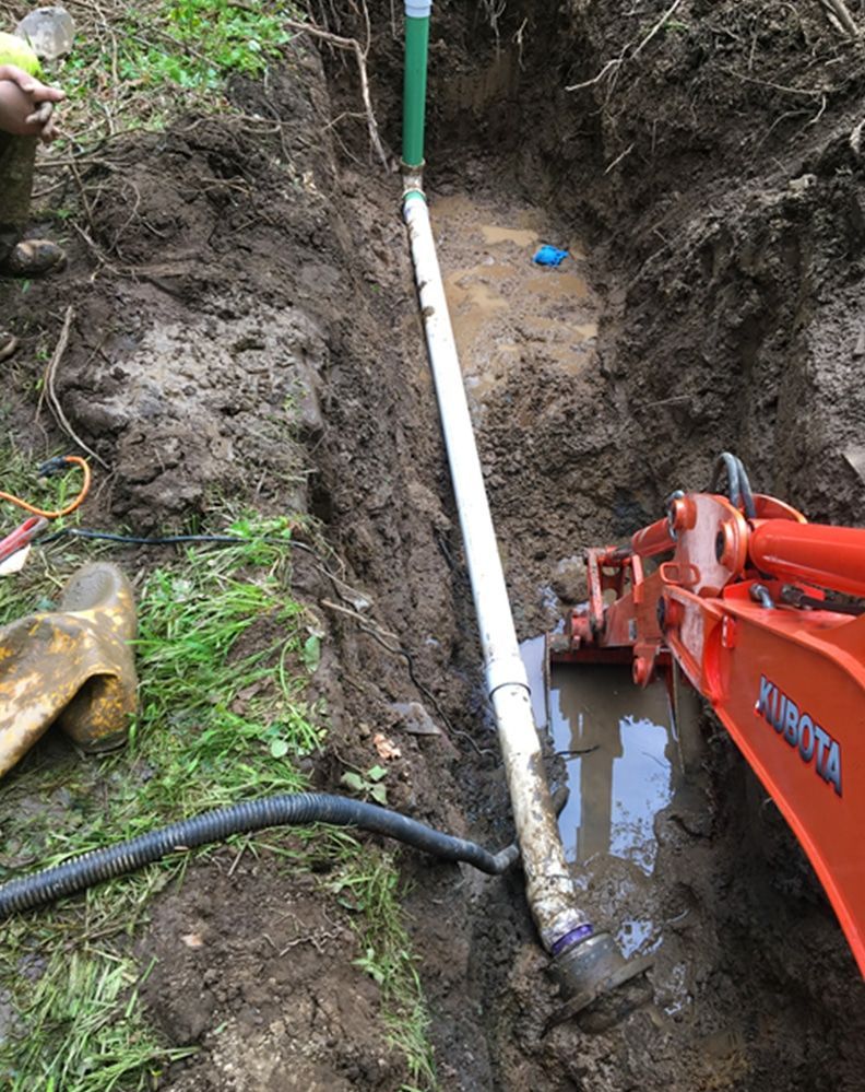 A pipe is being installed in a muddy hole next to a bulldozer.