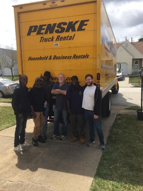 People standing in front of a yellow Penske moving truck on a sunny day.