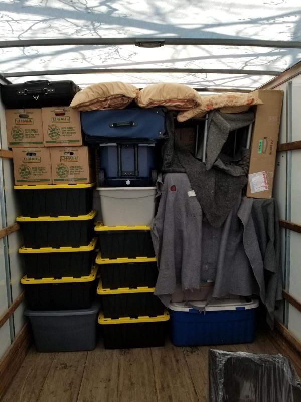 Moving truck interior packed with boxes, totes, luggage, clothing, and pillows.