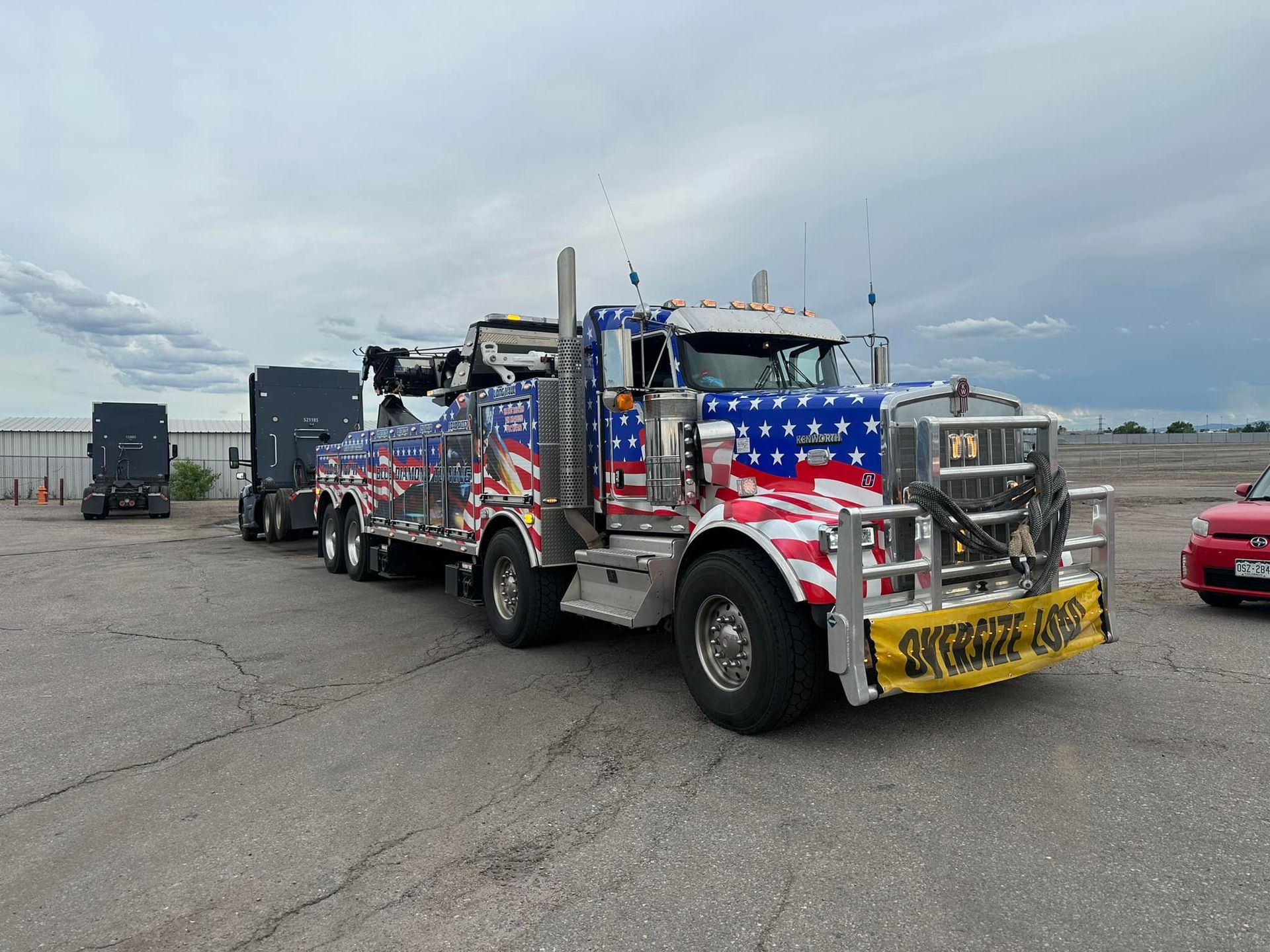 Patriotic-themed tow truck hauling a trailer in an industrial setting.