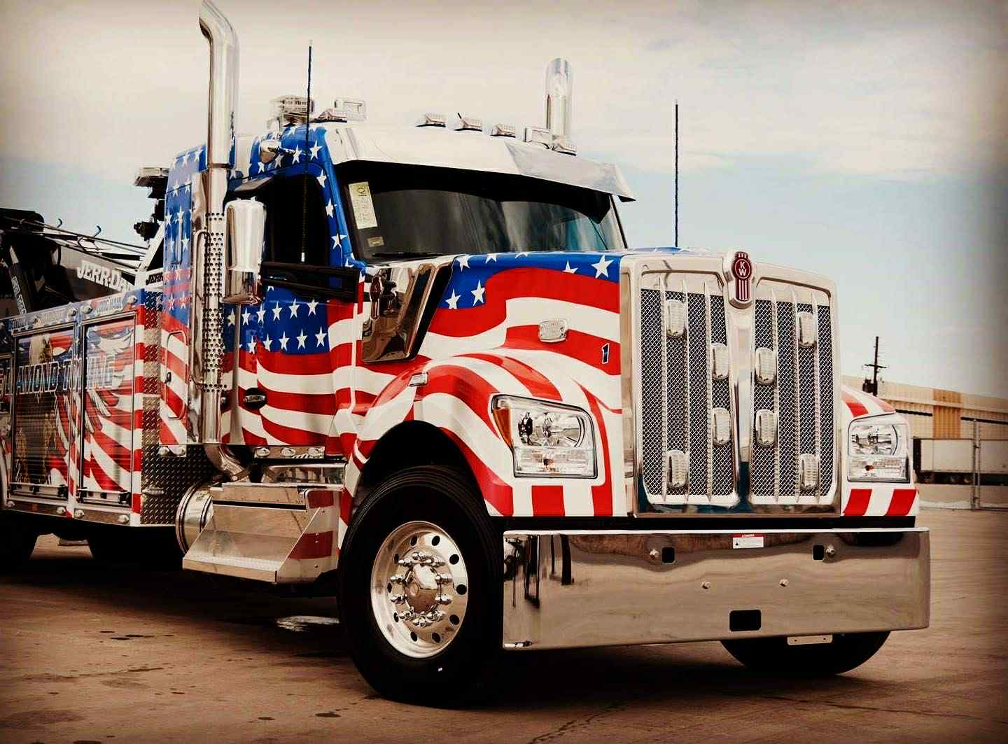 American flag-decorated tow truck parked outdoors. Patriotic red, white, and blue design on a Kenworth truck.