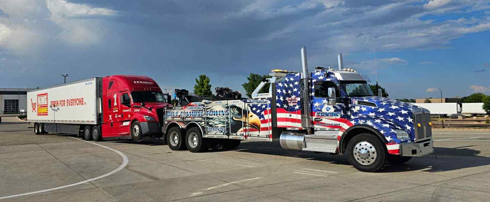 Tow truck with American flag design towing a red and white semi-truck.