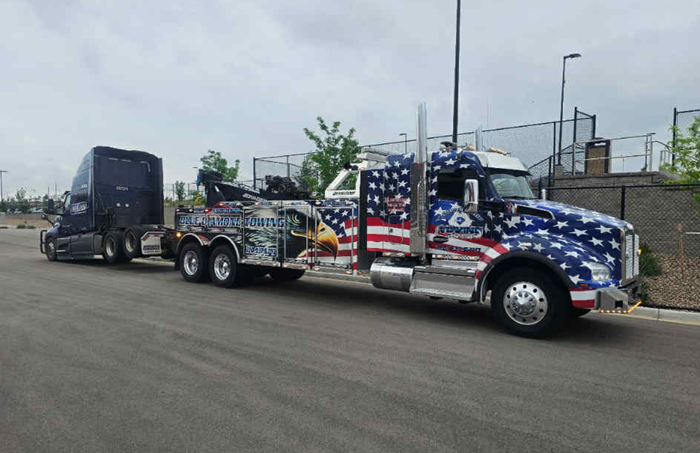 A patriotic tow truck pulling a semi-truck on a paved road.