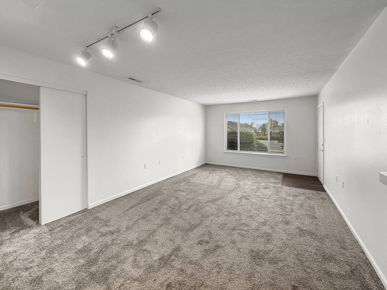 An empty bedroom with a large window and a closet.