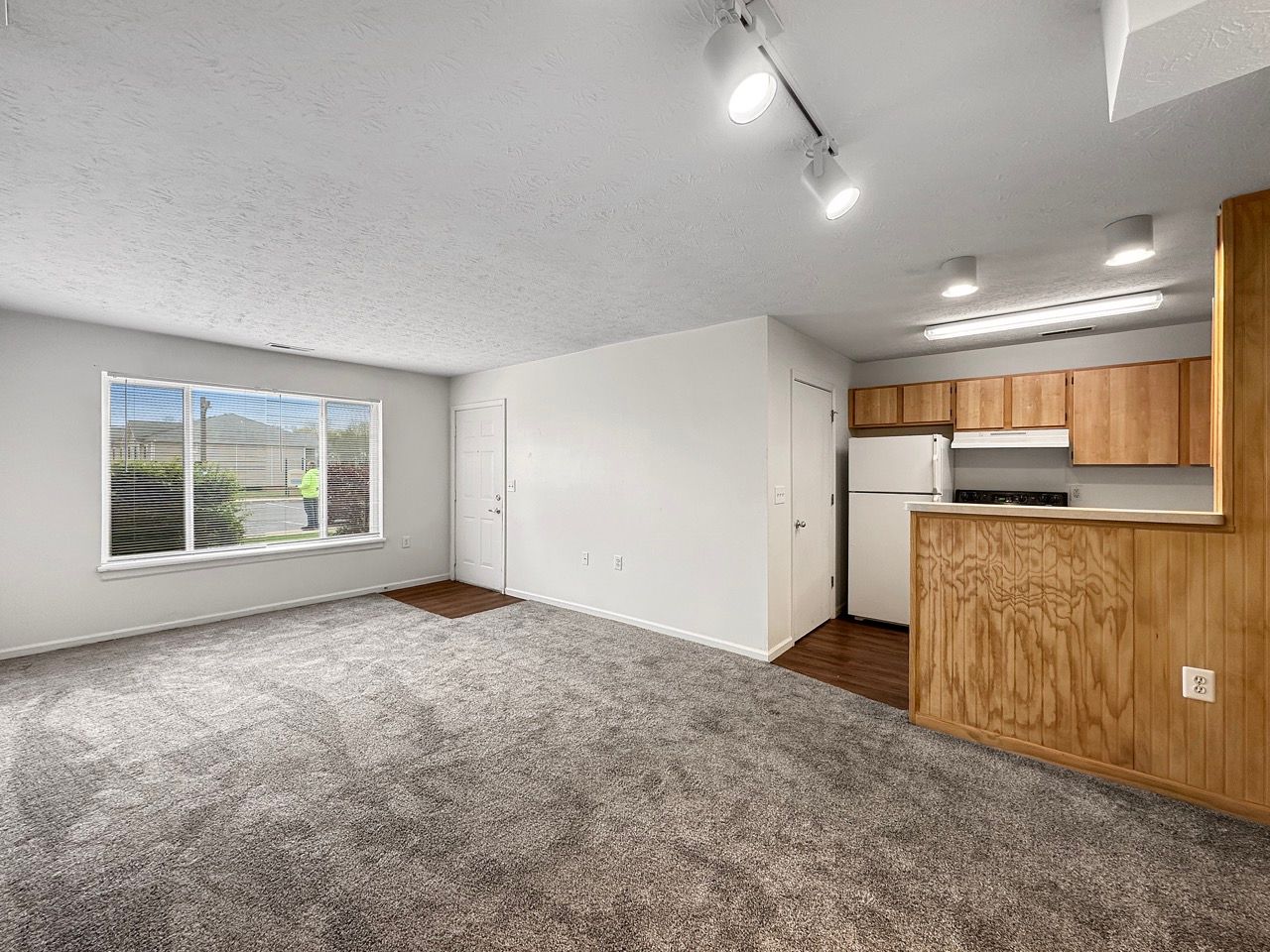 An empty living room with a large window and a kitchen.