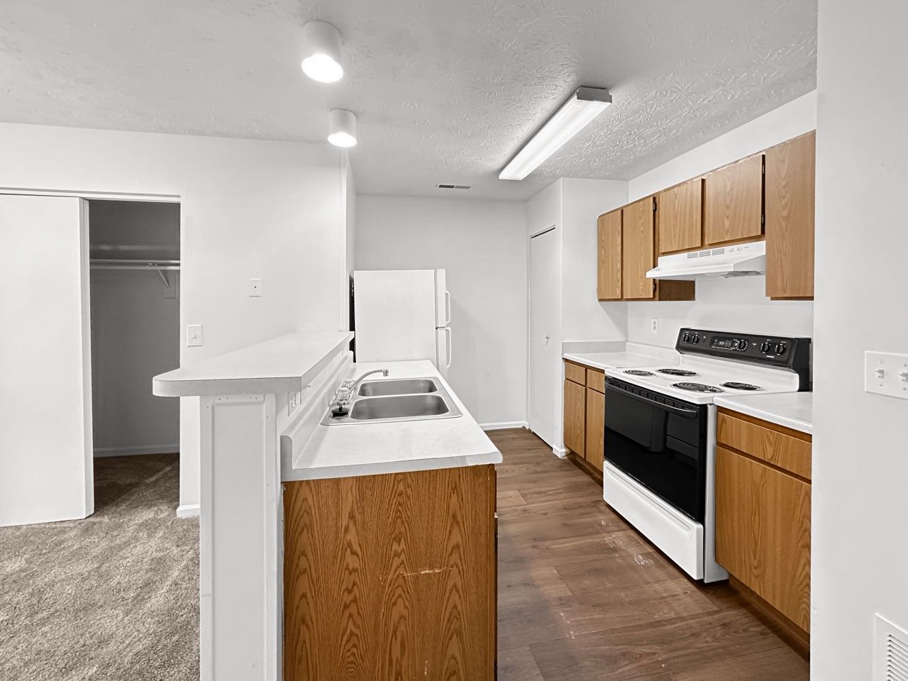 A kitchen with wooden cabinets , a stove , a refrigerator , and a sink.