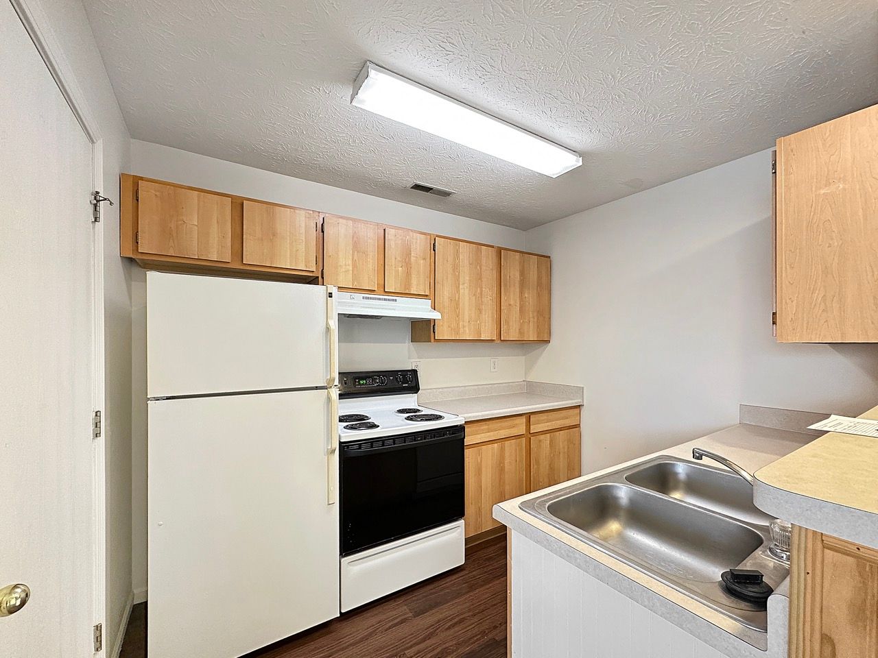 A kitchen with a stove , refrigerator , sink and wooden cabinets.