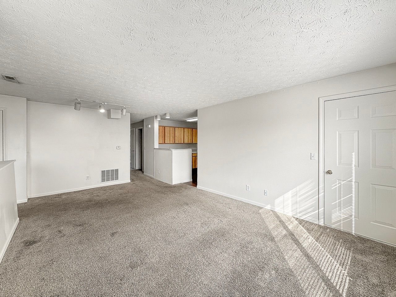 An empty living room with a carpeted floor and white walls.