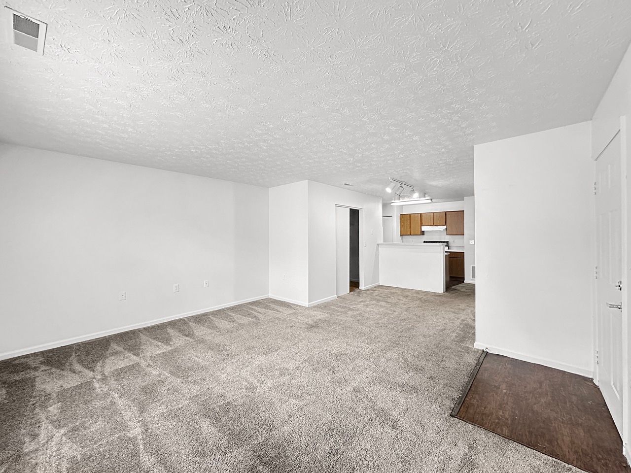 An empty living room with a carpeted floor and white walls.