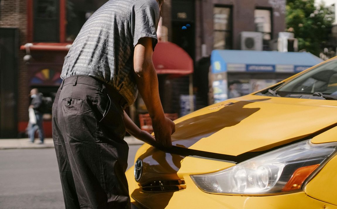 A man is working on a broken down car on the side of the road.