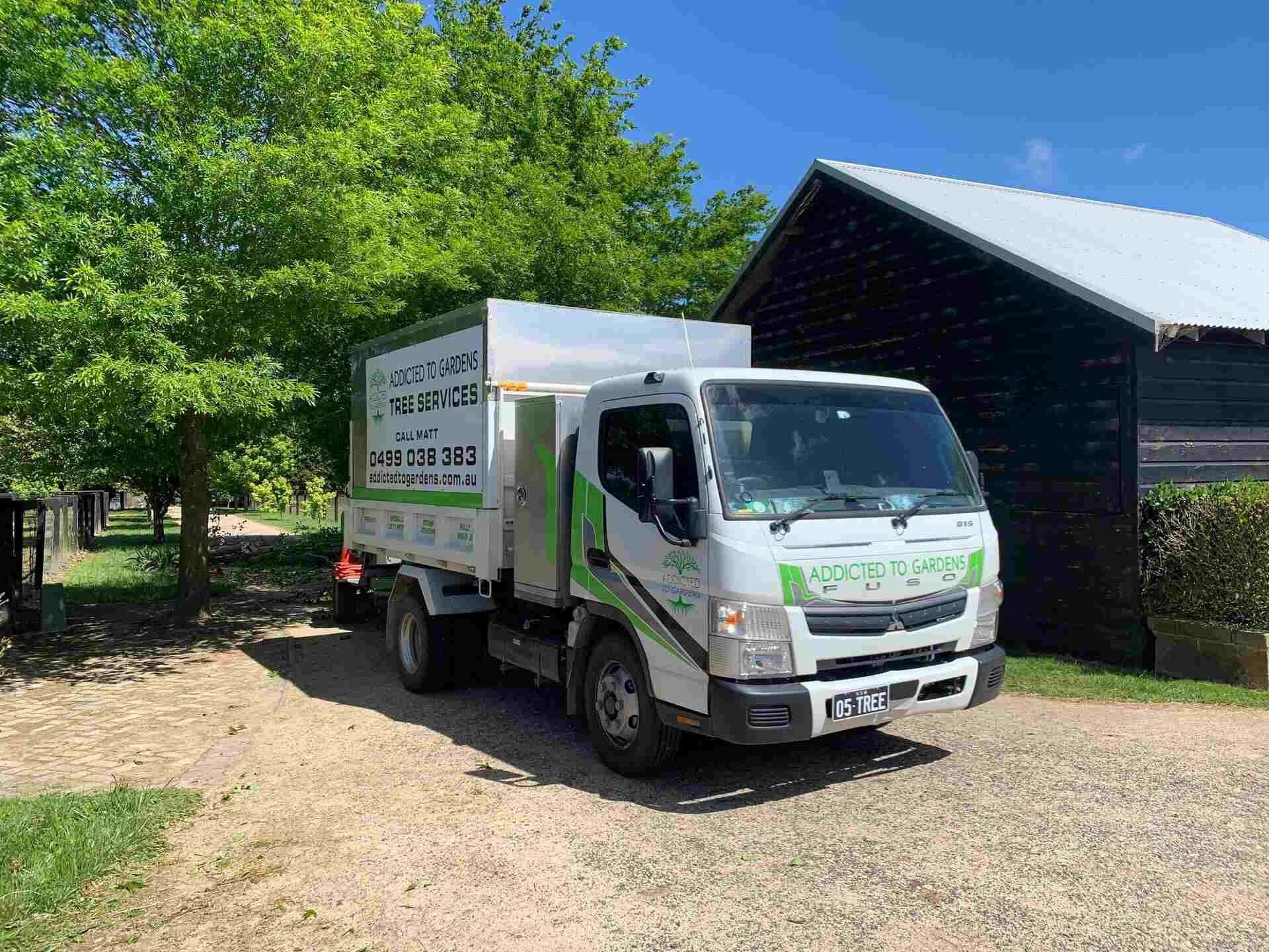 White truck with green trim parked on gravel near a dark barn and trees.