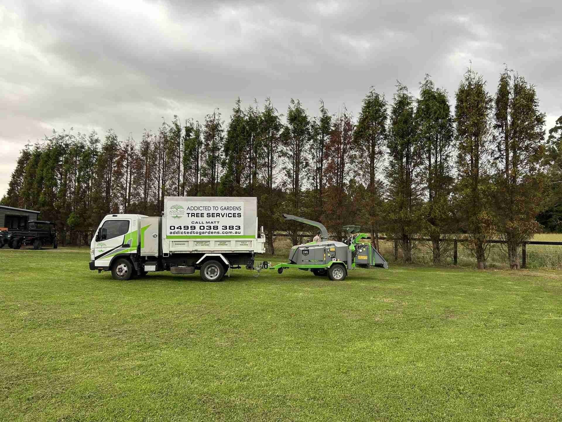 A truck with a chipper trailer on a grassy field; trees in background.