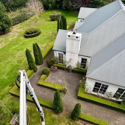 Aerial view of a house with a manicured yard, a long driveway, and boxwood hedges.