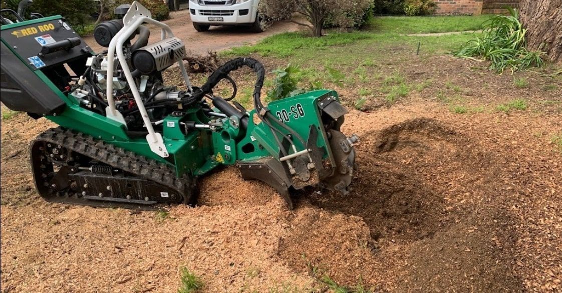 Green stump grinder on tracks grinding a tree stump in a yard.