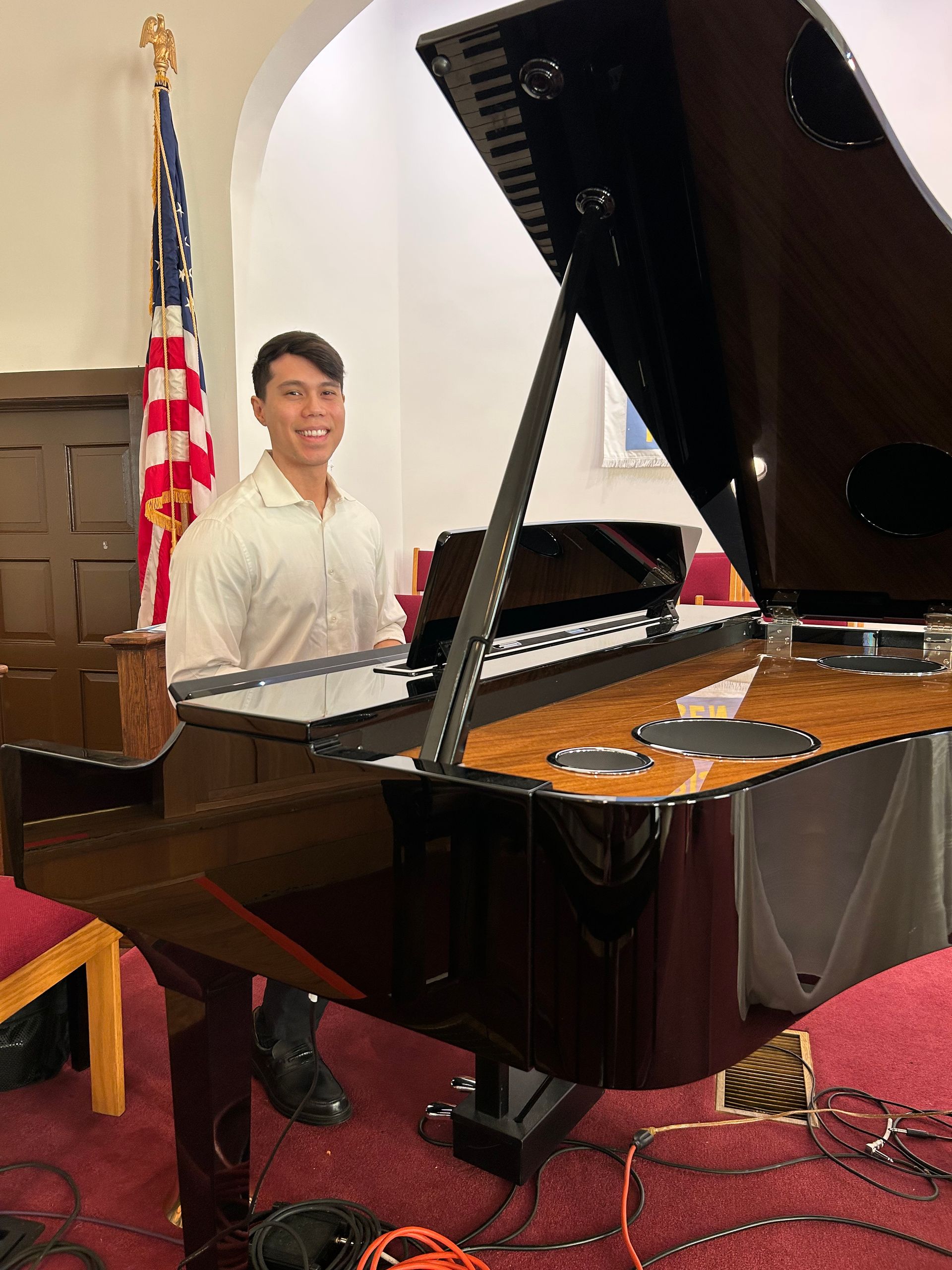 A pianist is playing a piano in a church with an american flag in the background