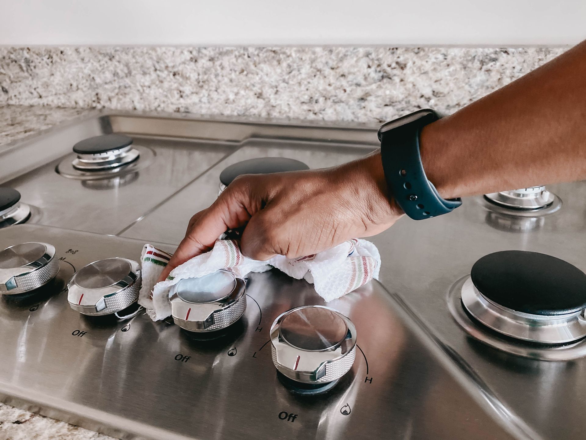 Person wiping a stainless steel stovetop with a cloth.